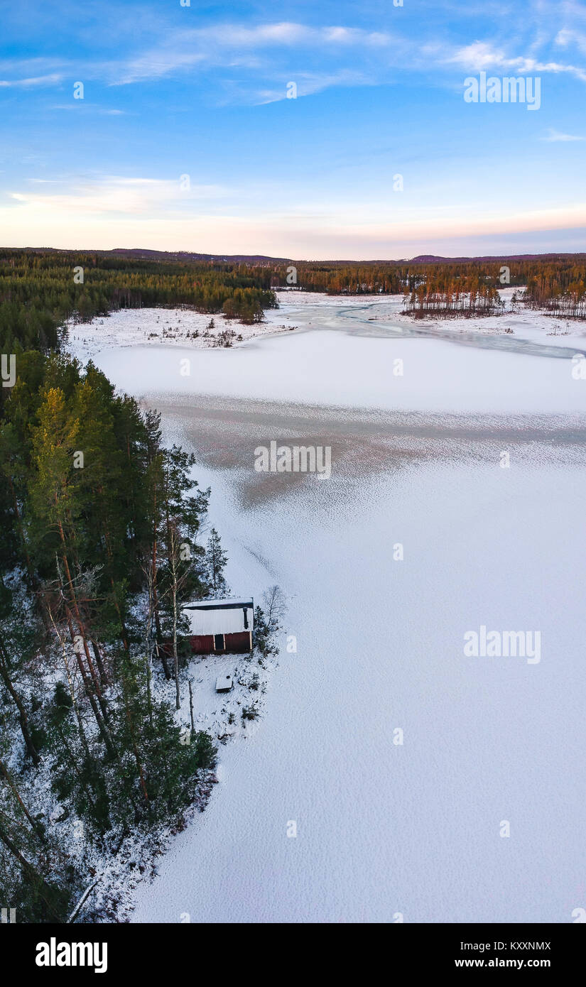 Kabine von einem gefrorenen Schwedischen See im Wald bei Sonnenuntergang. Mit einer Drohne im Winter fotografiert. Stockfoto