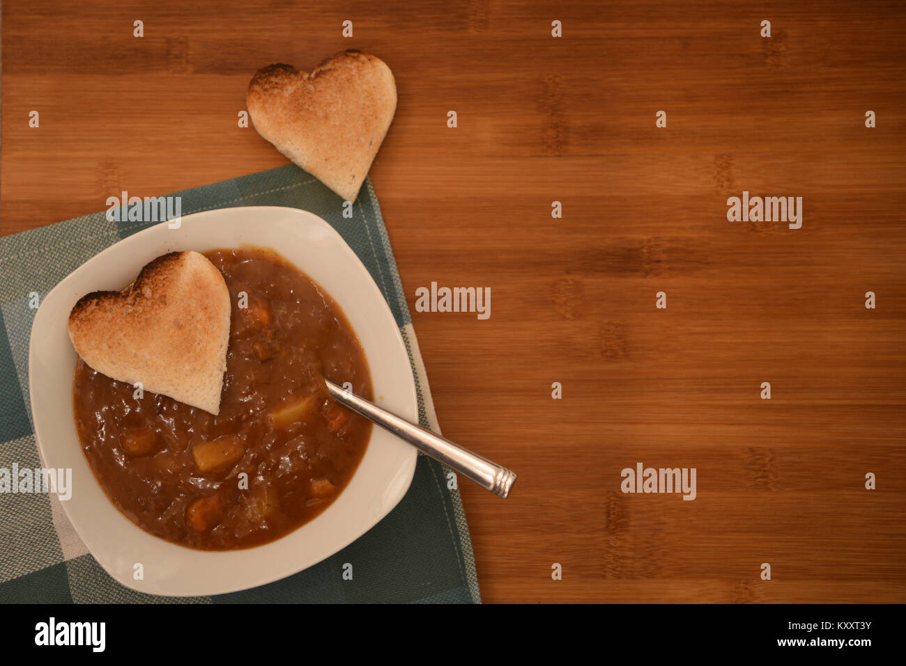 Essen Fotografie Bild von Huhn und Gemüse Suppe in einer weißen Schüssel und Löffel mit Liebe Herz Form Toast und grünen Tuch mit rustikalem Holz Hintergrund Stockfoto