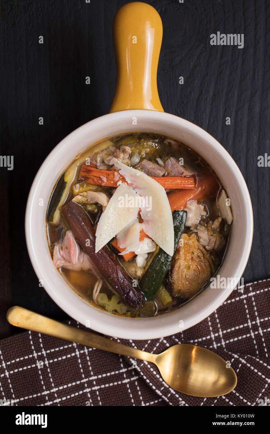 Schüssel Bunte Gemüsesuppe aus Zucchini, Karotten, Fleisch, Rosenkohl, Zwiebeln und Hühnerbrühe, serviert mit einem braunen gold Serviette und Löffel Stockfoto