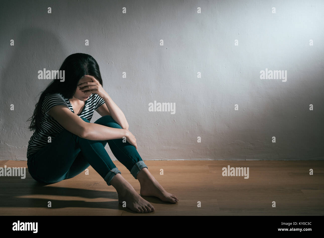 Schöne hübsche Frau in Depression bipolare Störung emotion Problem sitzen auf Holzboden in weiße Wand im Hintergrund. Stockfoto