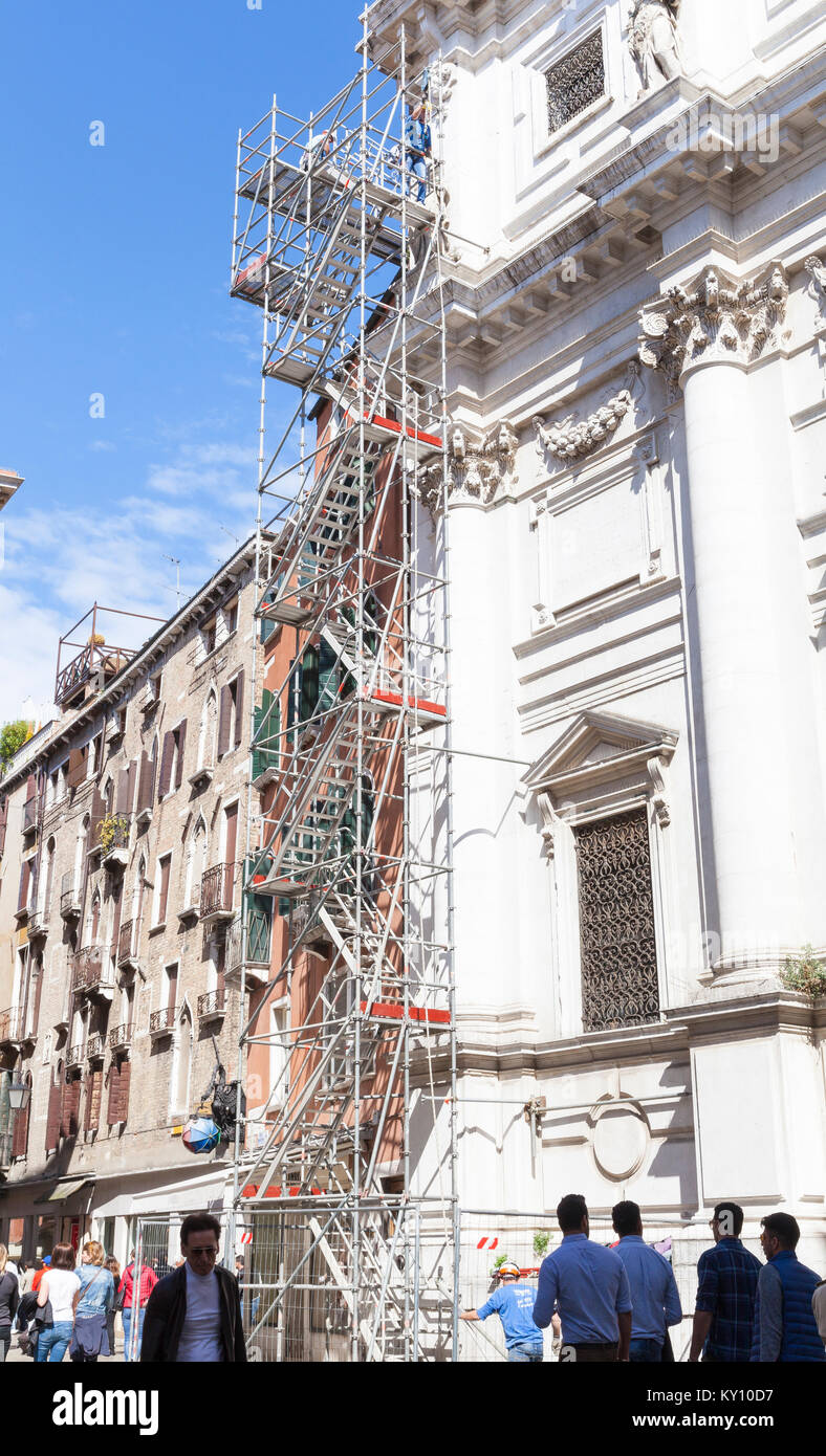 Instandhaltung der Gebäude in Venedig, Italien auf ein historisches Wahrzeichen mit Männern auf hohen dünnen Einrüstung der Fassade von Chiesa di San Salvador, Campo San Salv Stockfoto