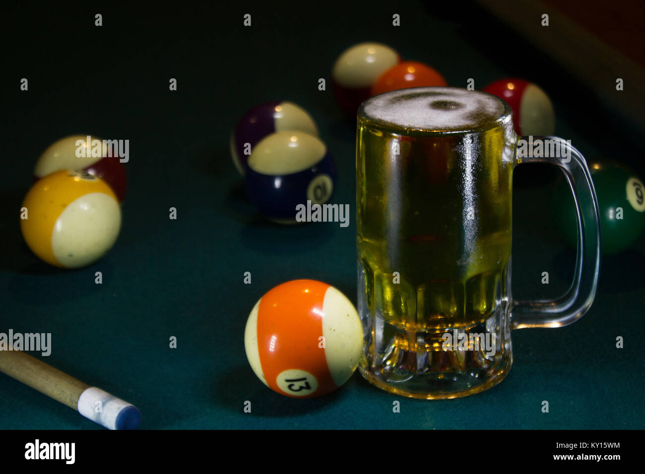 Kaltes Bier Becher auf einer grünen Billardtisch mit mehreren bunten Kugeln und Queue Stockfoto