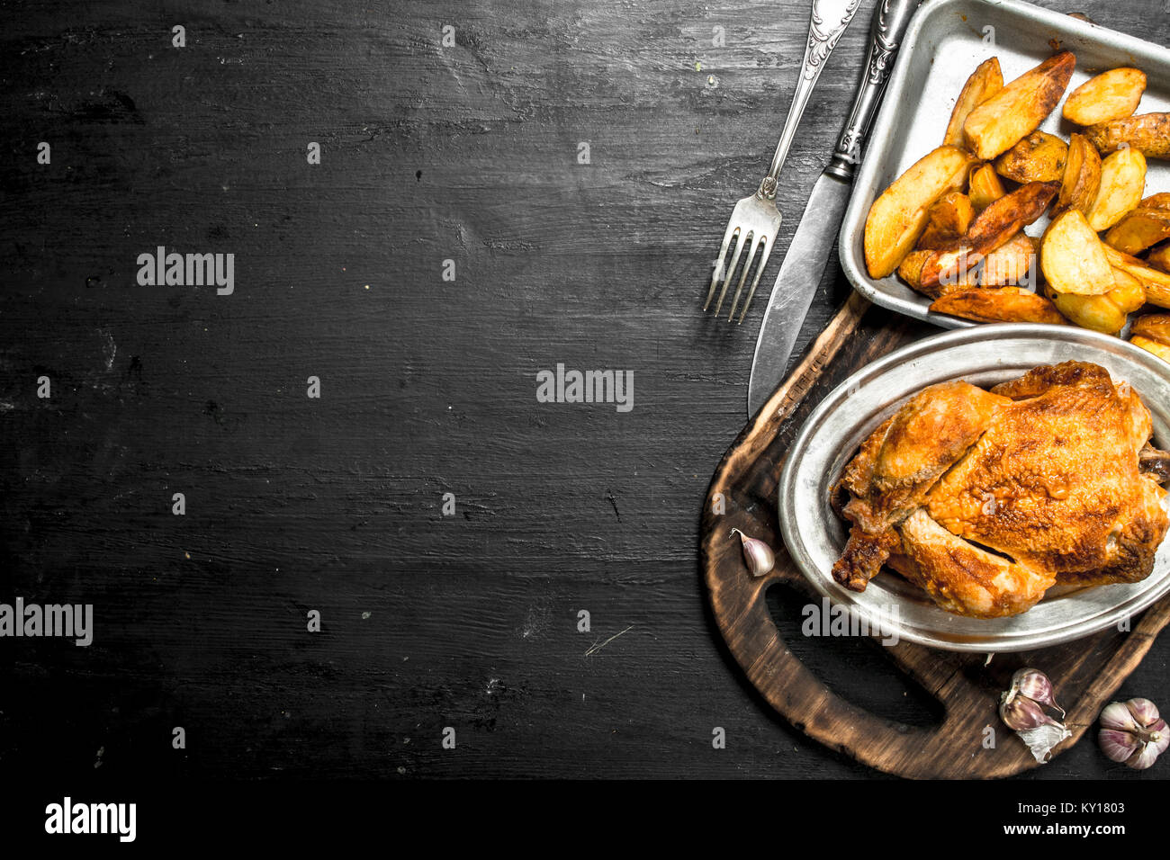 Gebratenes Huhn mit Kartoffeln auf ein Fach auf der schwarzen Tafel. Stockfoto