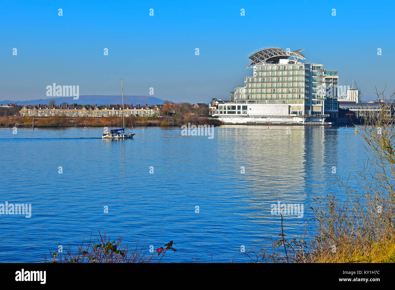 Eine kleine Yacht kehrt nach Hause zurück nach Cardiff Bay, vorbei an der St. David Hotel, ein 5 Sterne luxus Hotel durch den Auftraggeber Hotel Company. Stockfoto