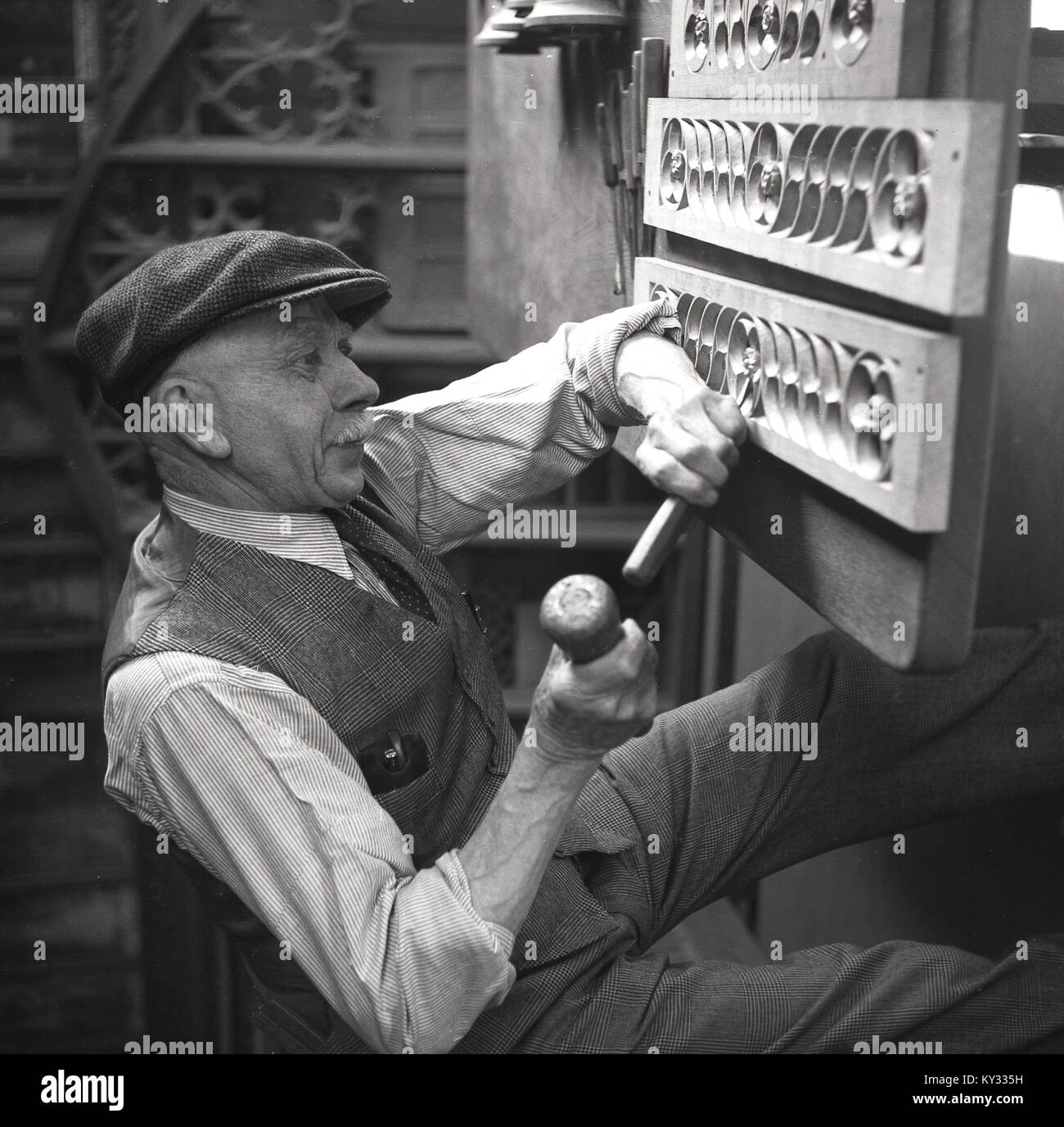 1950, historische, artisian Holzbearbeitung ... ein älterer Mann, der eine Weste, anzughosen und Klatschen mit einem Hammer und Meißel zu Carve out Formen auf Holzklötze über ihm fest, England, UK. Stockfoto