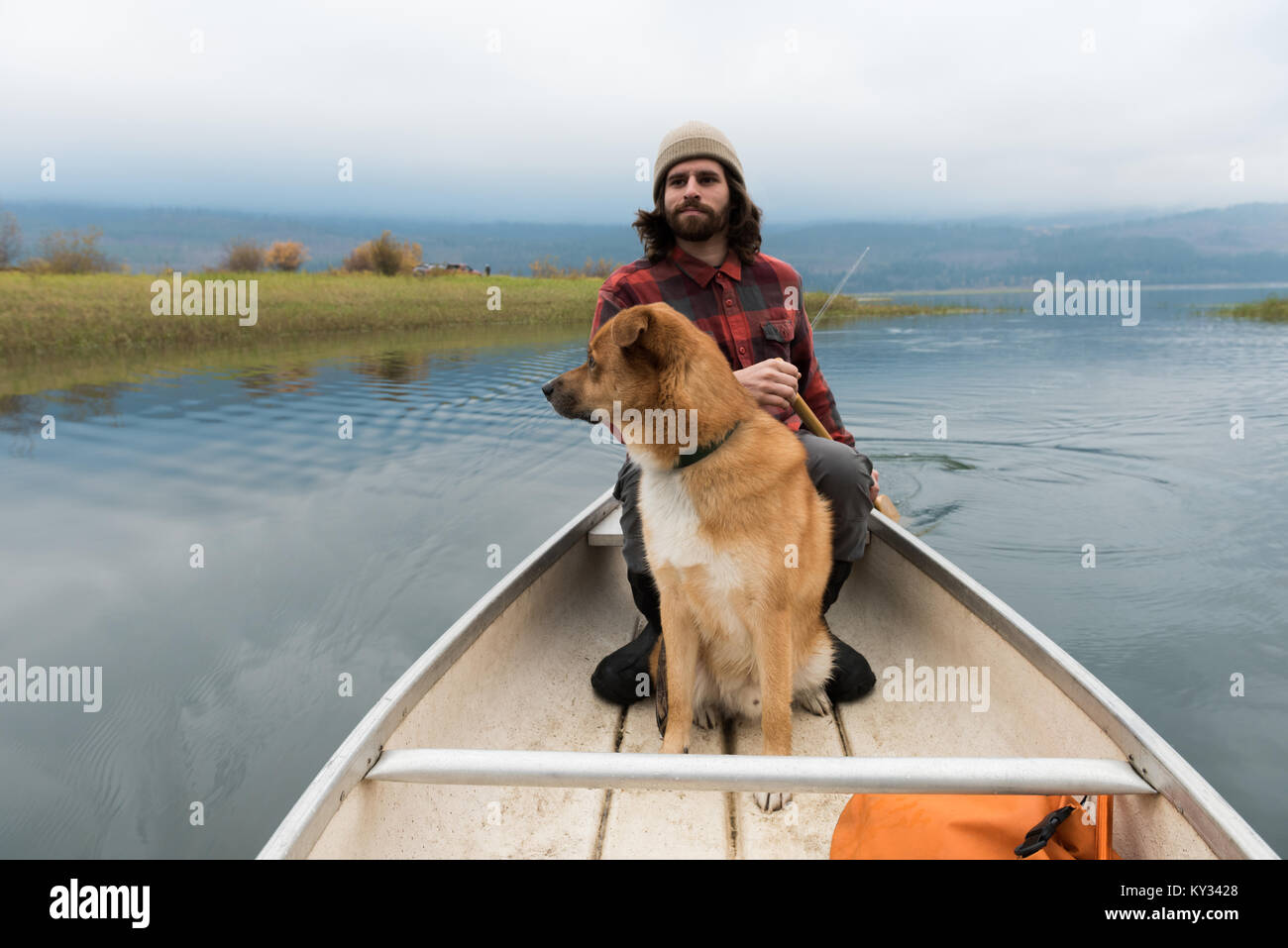 Mann oaring Kanu in Fluss mit seinem Hund an Bord Stockfoto