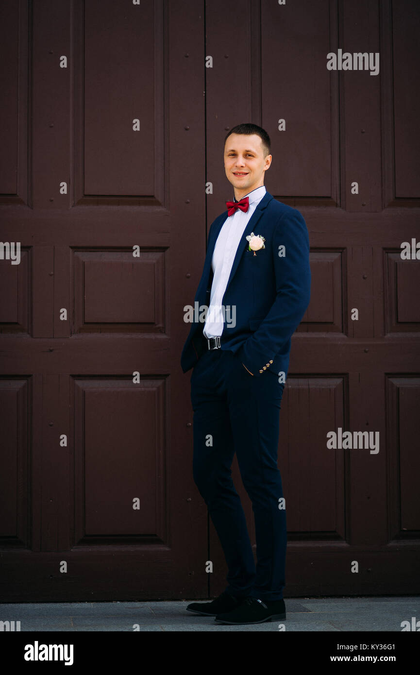 Bräutigam trägt blauen Anzug und Fliege an der roten Tür Stockfotografie - ...