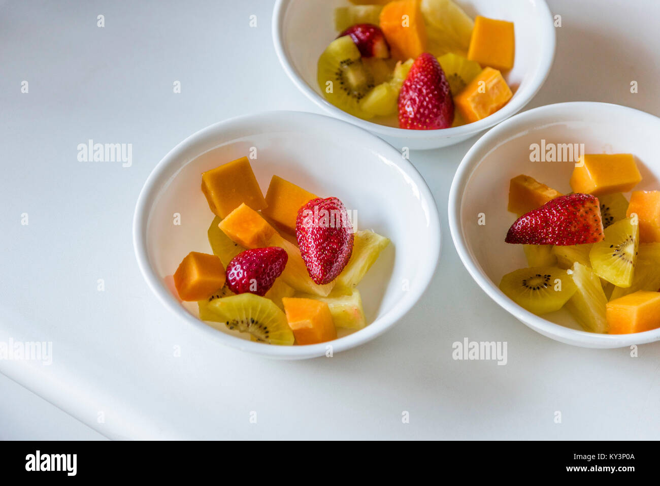 Bunter Salat von frischen Früchten in weißen Schalen, Ansicht von oben. Drei weiße Gerichte der Cut up gesundes Obst, weißer Hintergrund, Nahaufnahme. Stockfoto