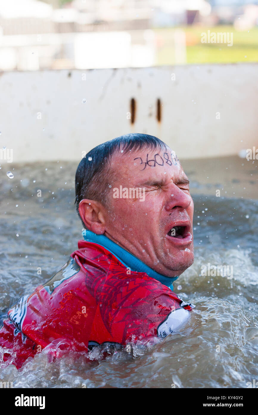 Sussex, UK. Ein Mann macht einen entsetzten Ausdruck, als er in einen Pool mit eiskaltem Wasser während einer haltbaren Mudder Fall stürzt. Stockfoto