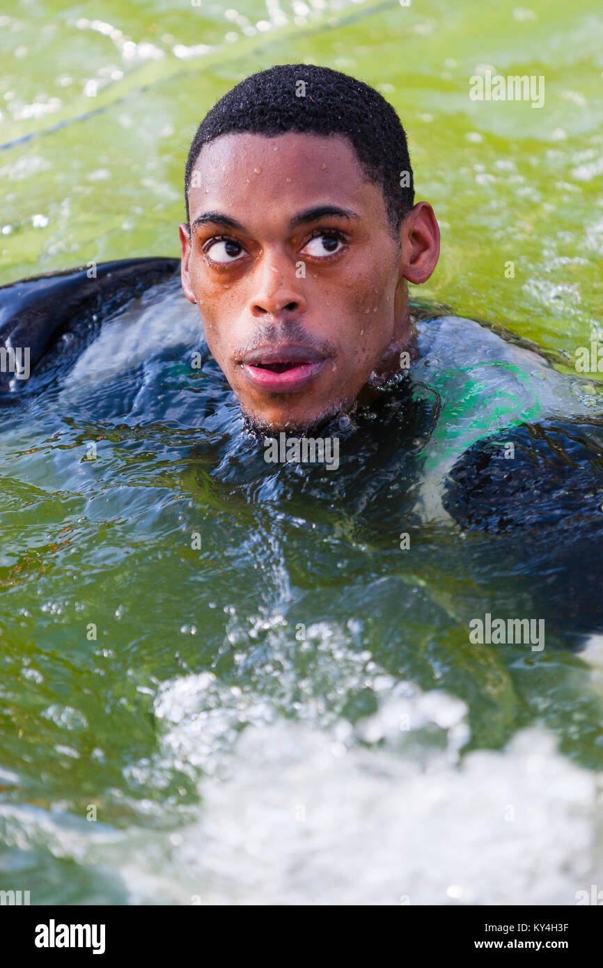 Sussex, UK. Ein männlicher Mitbewerber schwimmt an der Seite, nachdem Sie in das Wasser auf harten Hindernis der Hangin' während einer haltbaren Mudder Ereignis. Stockfoto