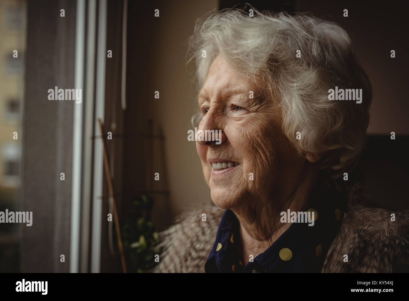 Lächelnde ältere Frau auf der Suche aus dem Fenster Stockfoto