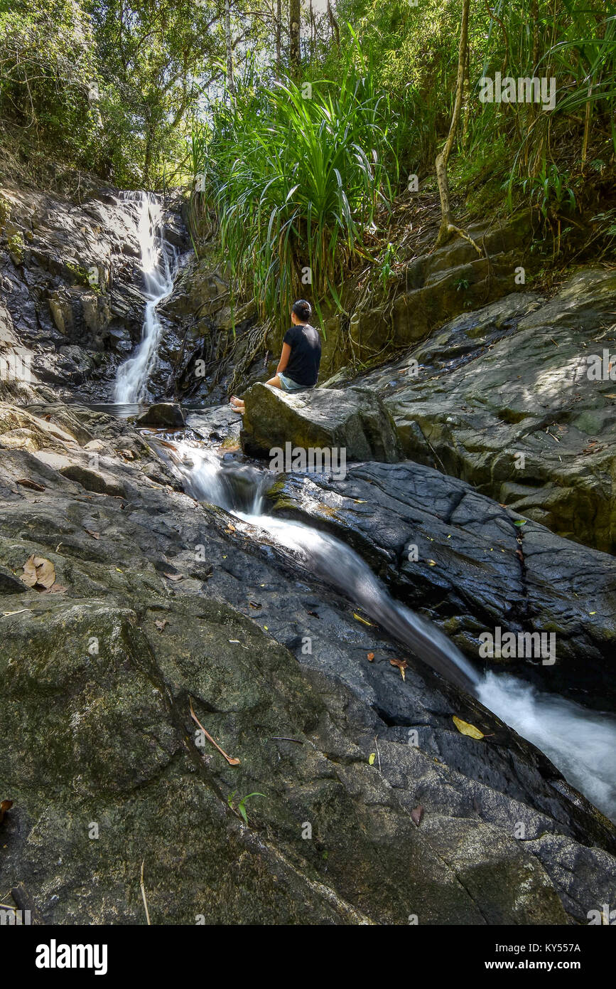 Junge Frau saß auf Felsen eine Dschungel-Wasserfall-Betrachtung zu betrachten. Stockfoto