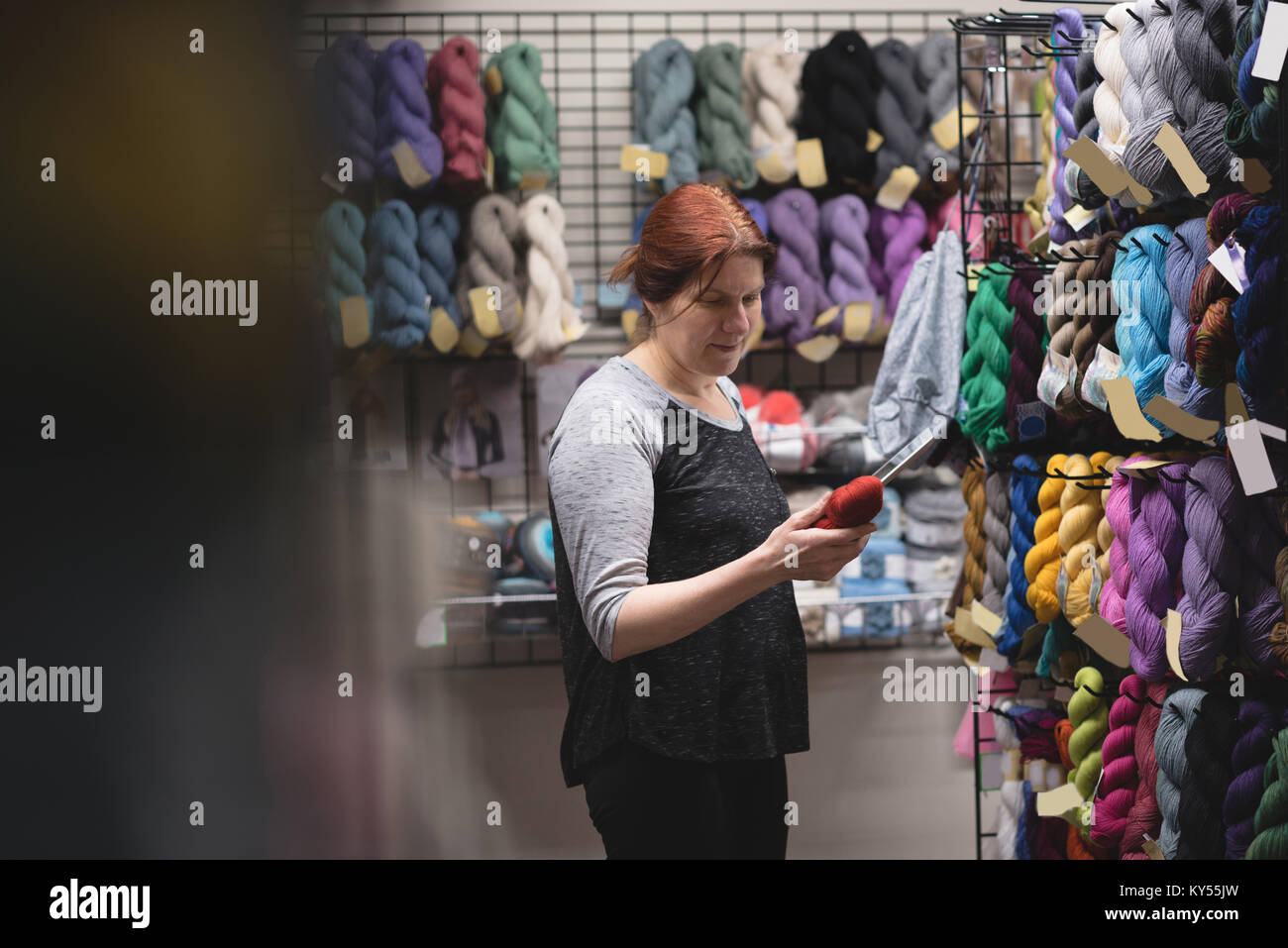 Frau auf der Suche nach Garn während der Verwendung digitaler Tablet Stockfoto