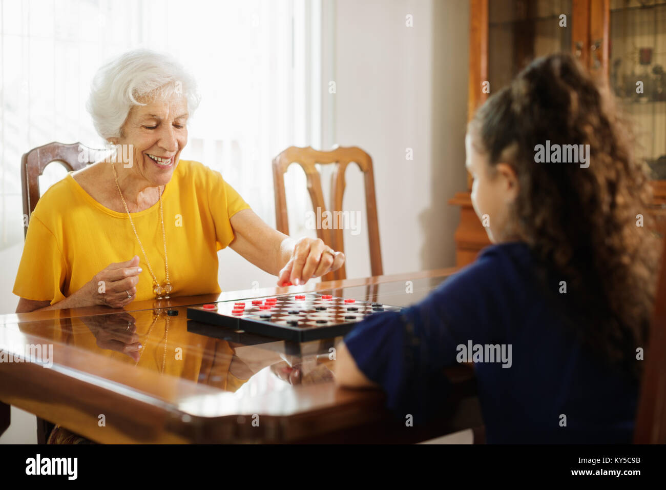 Glückliche kleine Mädchen spielen Checkers mit älteren Frau zu Hause. Familie Beziehung mit Großmutter und Enkelin. Oma und Enkel wi Stockfoto