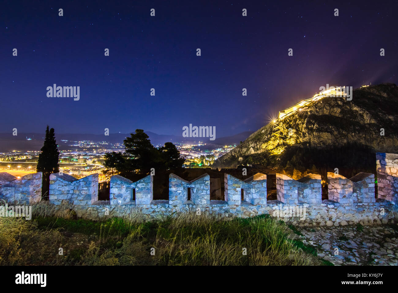 Beleuchtete Altstadt von Nafplion in Griechenland mit Ziegeldächern, kleinen Hafen, bourtzi Burg, Festung Palamidi in der Nacht. Stockfoto