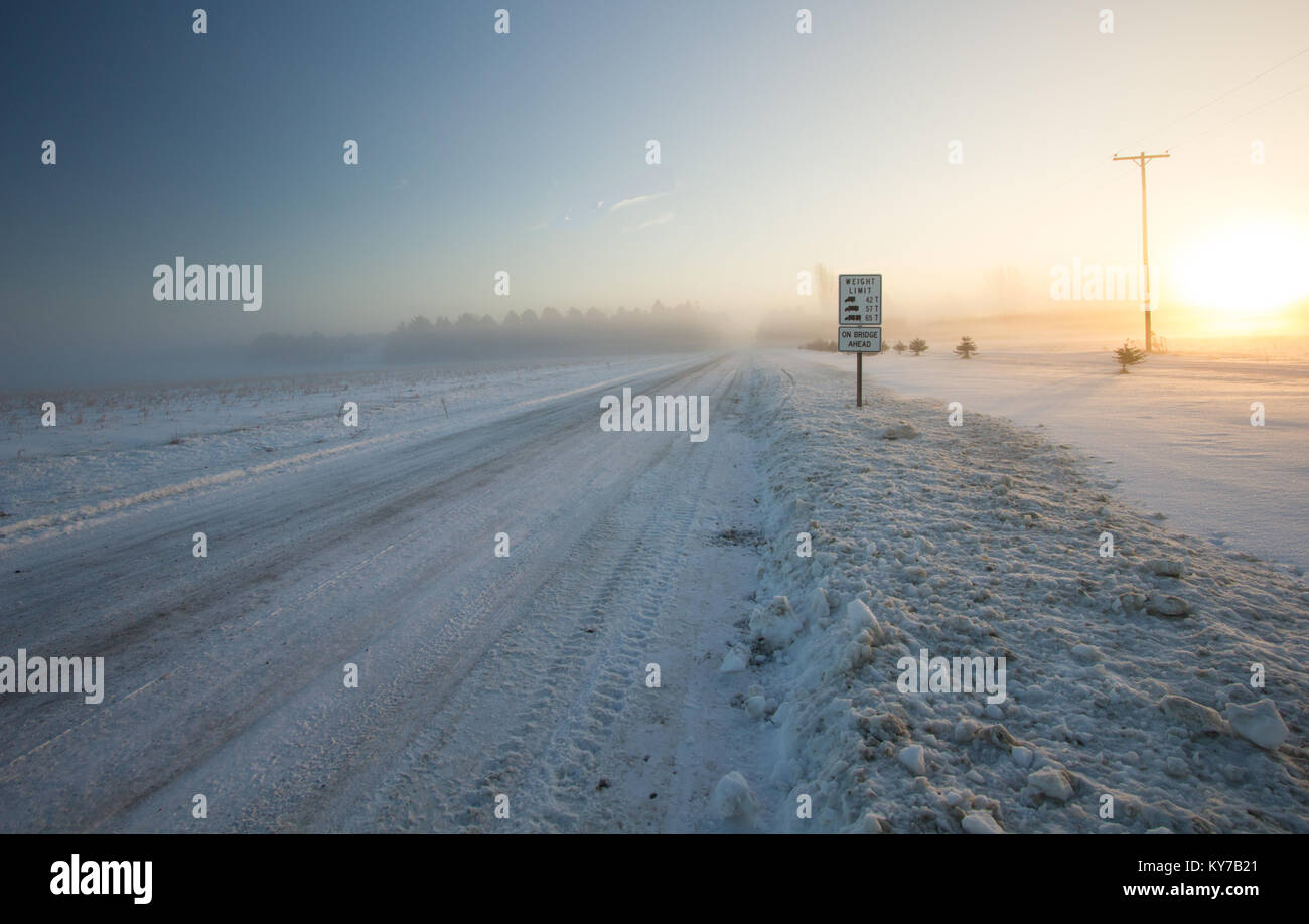 Einsatz im Winter Hintergrund. Ländliche Land verschneite Straße mit einem kalten Winter Schnee Wind weht über den Horizont. Stockfoto