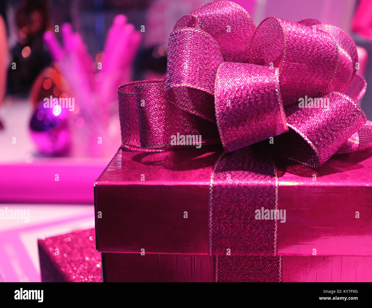 Geschlossen bis ein Quadrat glänzend leuchtend rosa Geschenkkarton mit Streuer vivid Pink Ribbon Bow, selektiver Fokus, verschwommenen Hintergrund Stockfoto