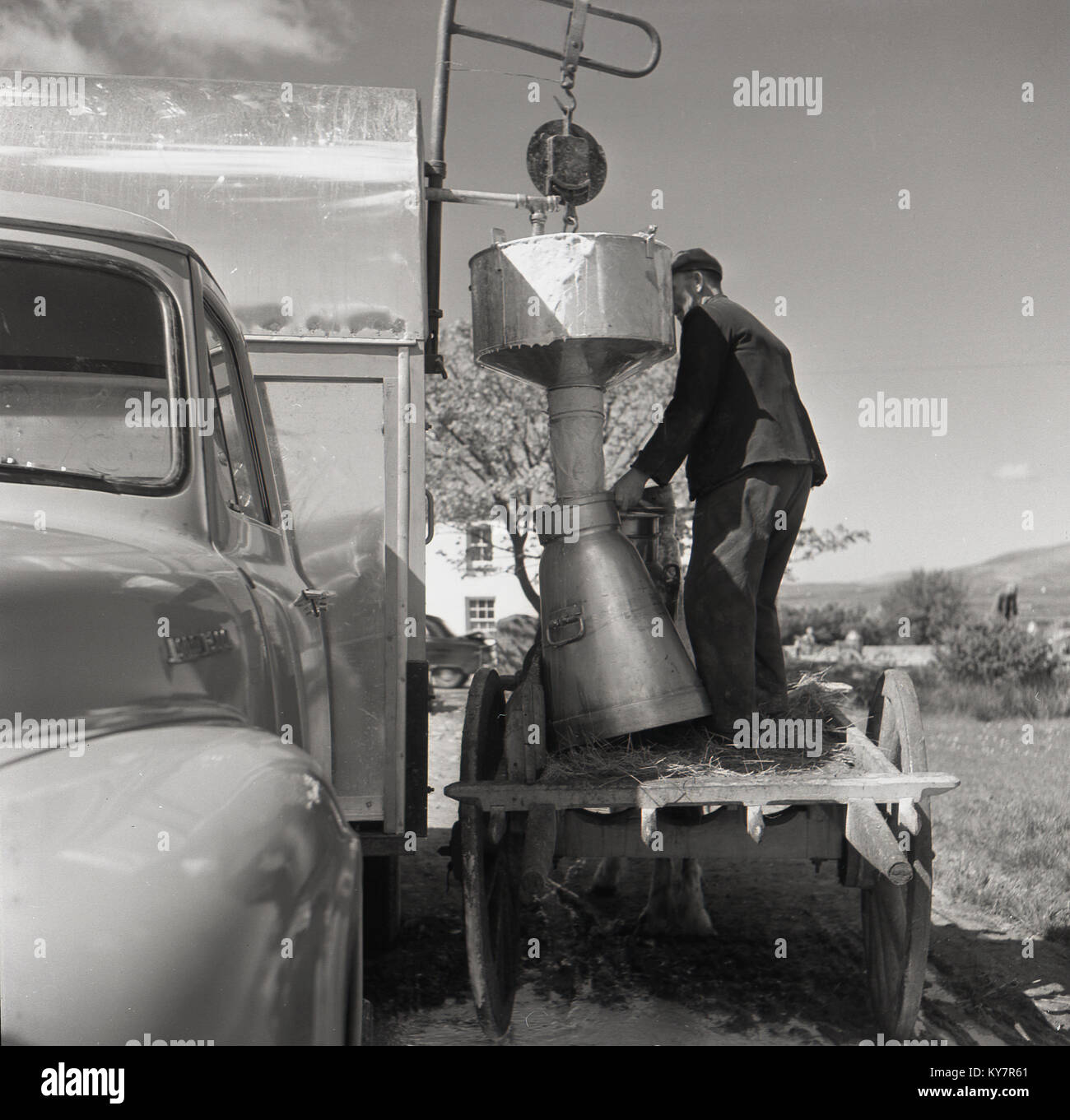 1950, historische, Mann auf dem Rücken eines Holz- Warenkorb füllen, ein Metall Milchkanne mit frischer Milch aus einem Spender hängen von einem mobilen Van, Irland. Stockfoto