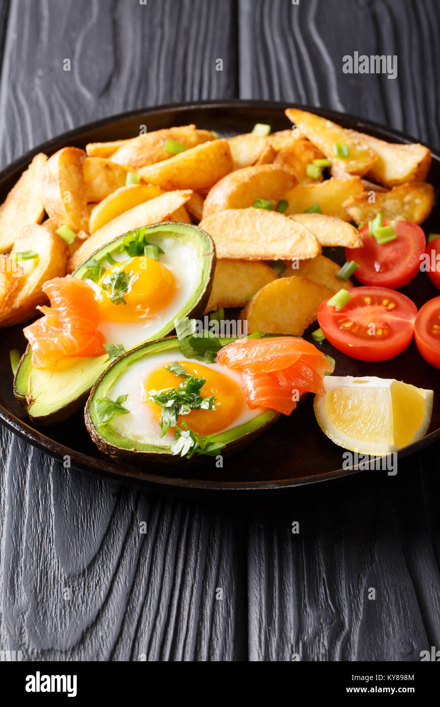 Leckeres essen: gebackene Avocado mit Ei und Lachs, frische Tomaten und Kartoffeln in der Nähe gefüllt - bis auf einen Teller auf dem Tisch. Vertikale Stockfoto