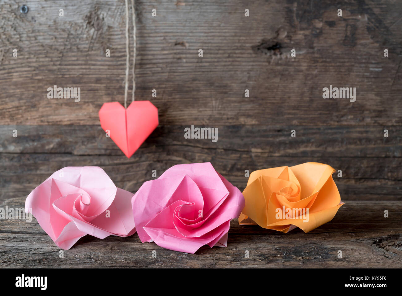 Origami Papier Blumen in Rot, Rosa und Orange für den Valentinstag vor der Weiche konzentrieren Papier rot Herz aus Papier hängen von Braun Garn gegen Rost Stockfoto