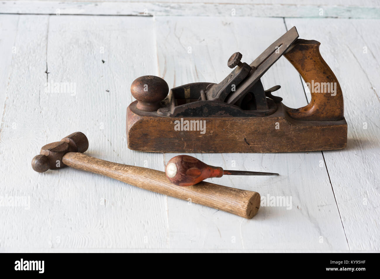 Sammlung von antiken, verwitterte vintage Tools, Hammer, Awl und Holzklotz Ebene, gegen verwitterten weiß lackierten Holz Hintergrund Stockfoto