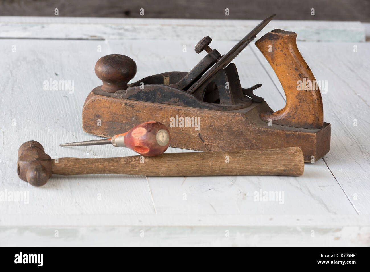 Nahaufnahme der Sammlung von antiken, verwitterte vintage Tools, Hammer, Awl und Holzklotz Ebene, gegen verwitterten weiß lackierten Holz Hintergrund Stockfoto