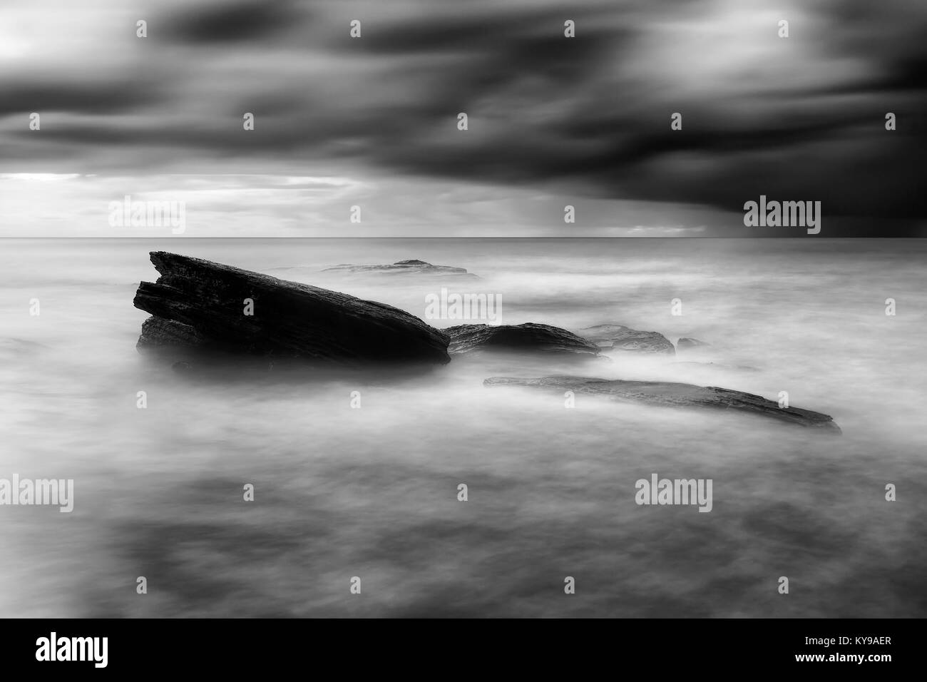 Dunkle stürmische Wetter Bungan Strand von Sydney Northern Beaches mit massiven schwarzen Felsbrocken Felsen stehend aus Unscharf surfen Wasser des Pazifischen Ozeans. Stockfoto