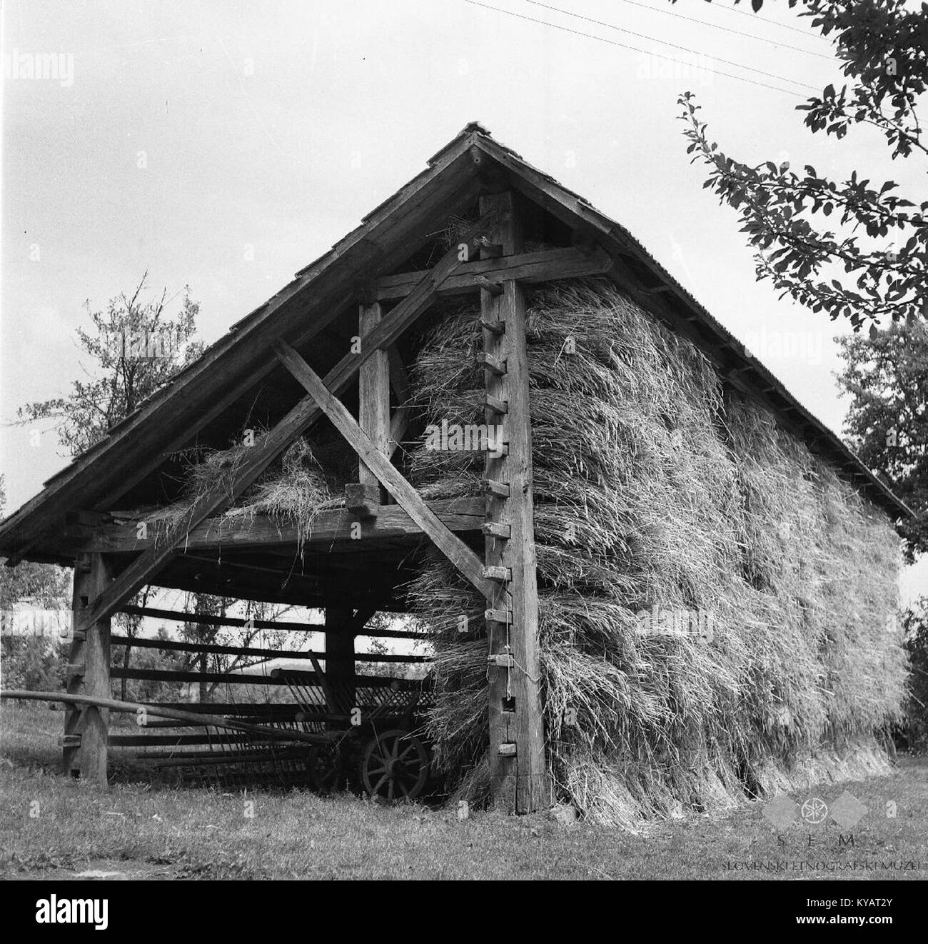Das Foto von 1964 zeigt einen Kozolec, eine traditionelle slowenische Heuhacke mit Dachkonstruktion, die sich in der Nähe einer Eisenbahn befindet und beispielhaft für die landwirtschaftliche Architektur ist. Stockfoto
