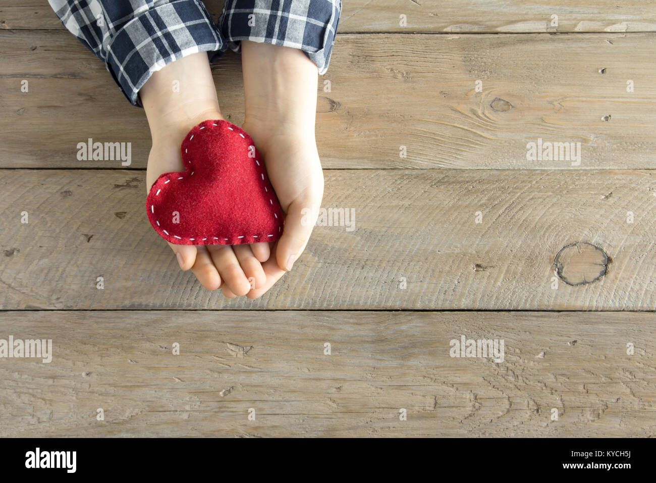 Rotes Herz in Kind Hände über Holz- Hintergrund, kopieren. Güte, Liebe und Nächstenliebe Konzept, hand made Valentinstag Geschenk. Stockfoto