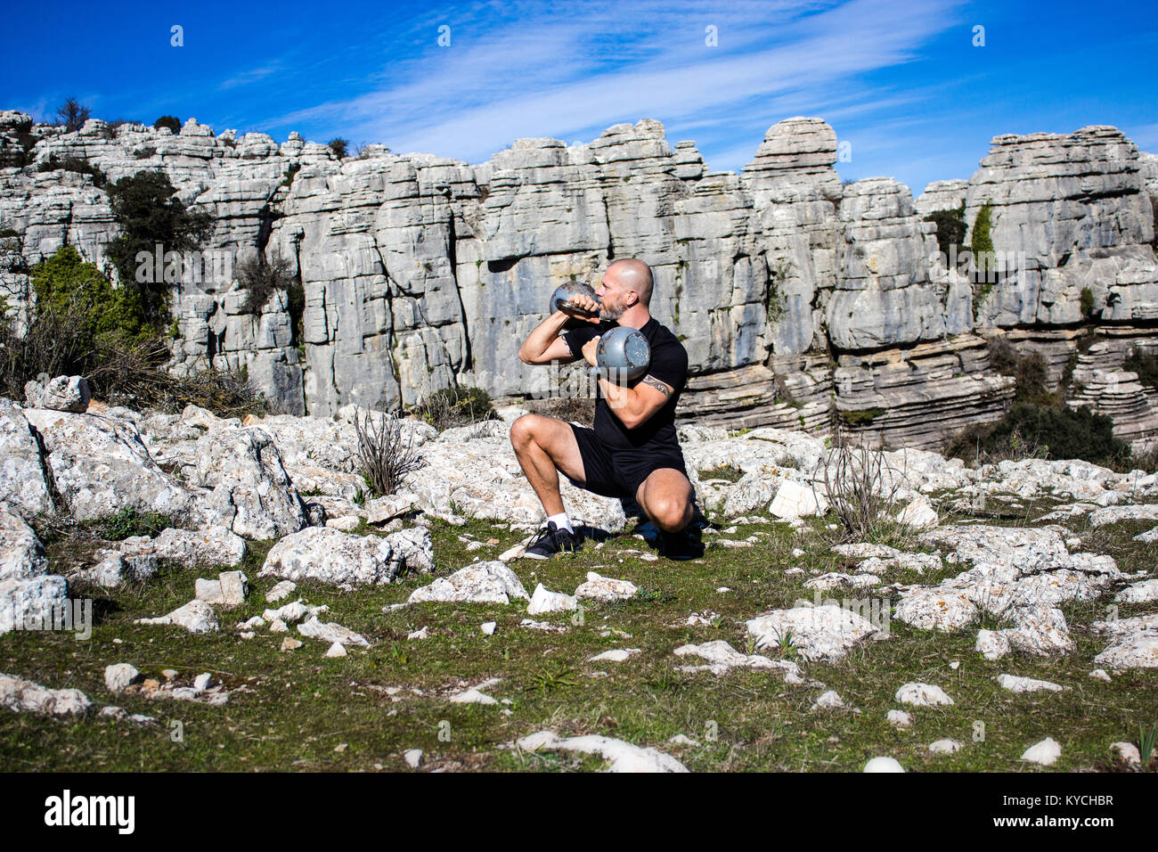 Man geduckt halten zwei Kettlebells in felsigem Gelände Stockfoto