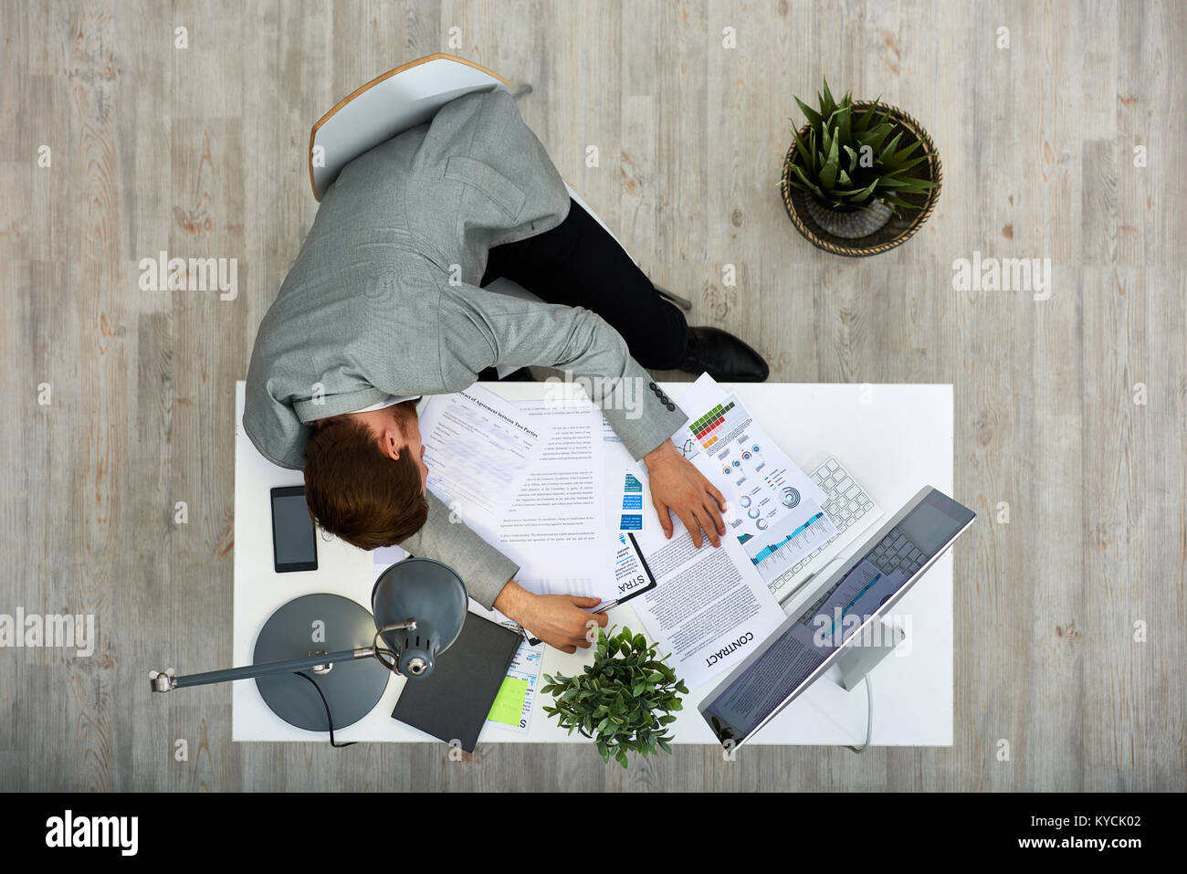 Müde junge weiße Arbeiter unter nap beim Sitzen am Schreibtisch mit Dokumenten behandelt, direkt oberhalb der Ansicht Stockfoto