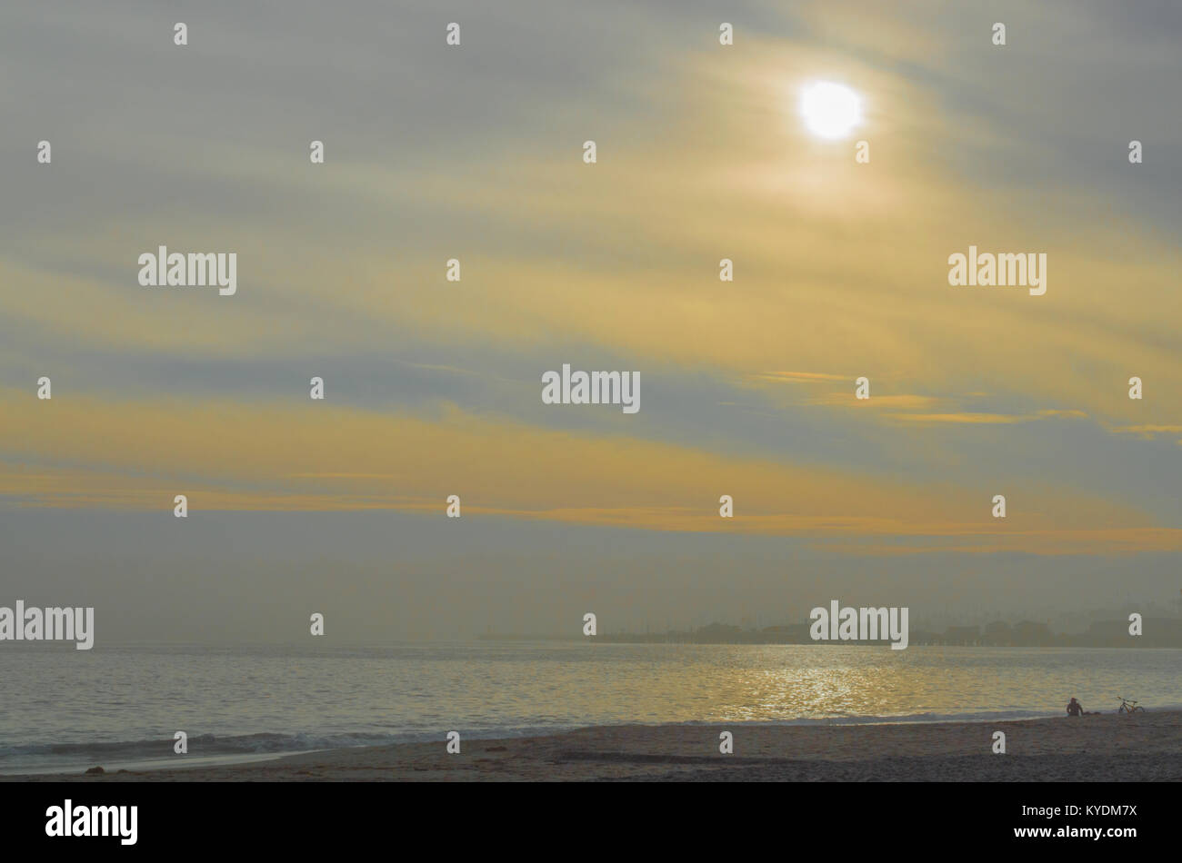 Golden, rauchiger Himmel mit Sonne schimmernden auf dem Ozean und eine einsame Person am Strand in Santa Barbara, Kalifornien, USA Stockfoto