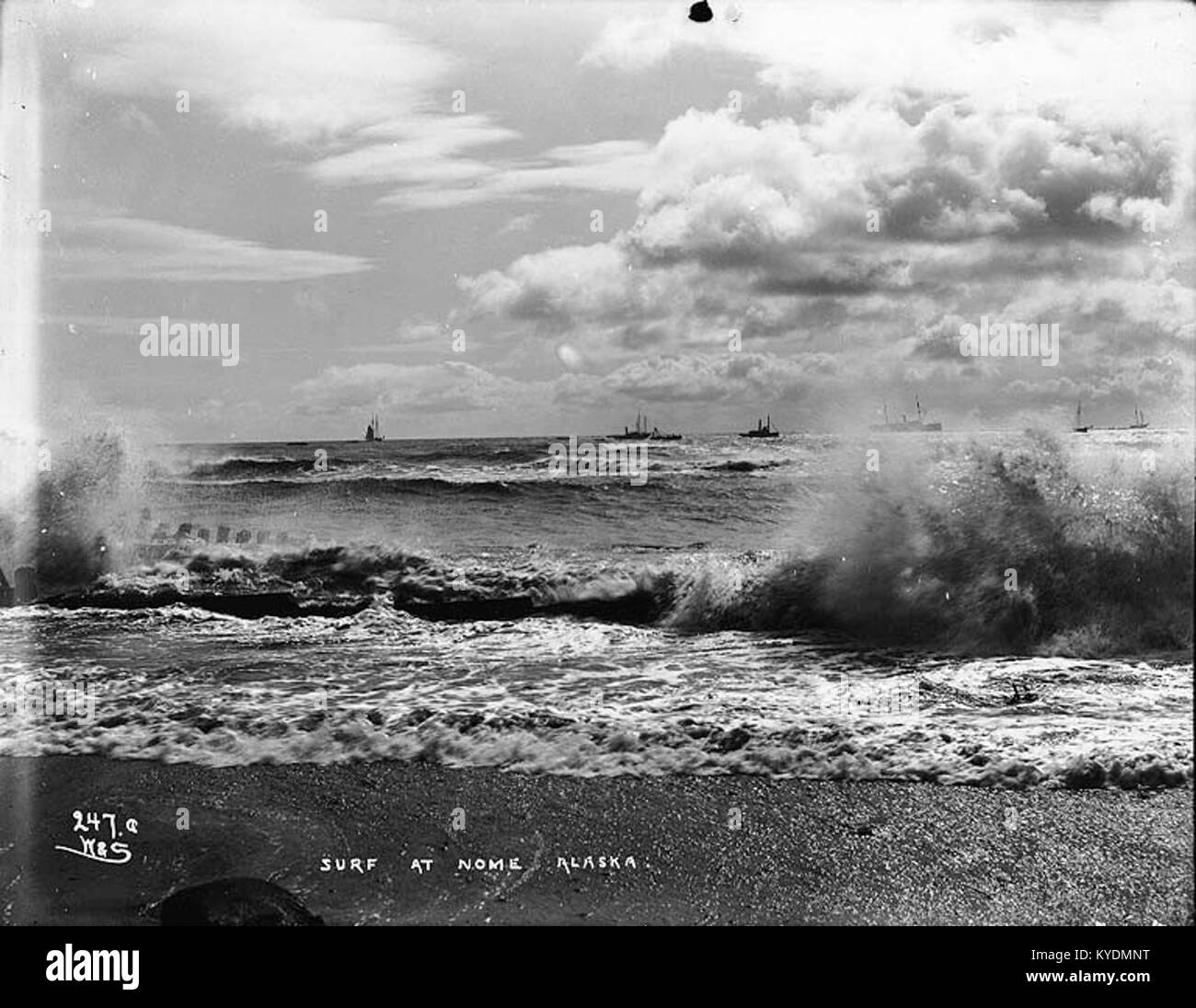 Das Foto wurde um 1900 aufgenommen und zeigt Schiffe, die vor der Küste in Nome, Alaska, ankerten, wobei während der Nome Gold Rush-Ära Wellen entlang der Küste brachen, was den Seeverkehr und die Küstenaktivitäten im Westen Alaskas veranschaulicht. Stockfoto