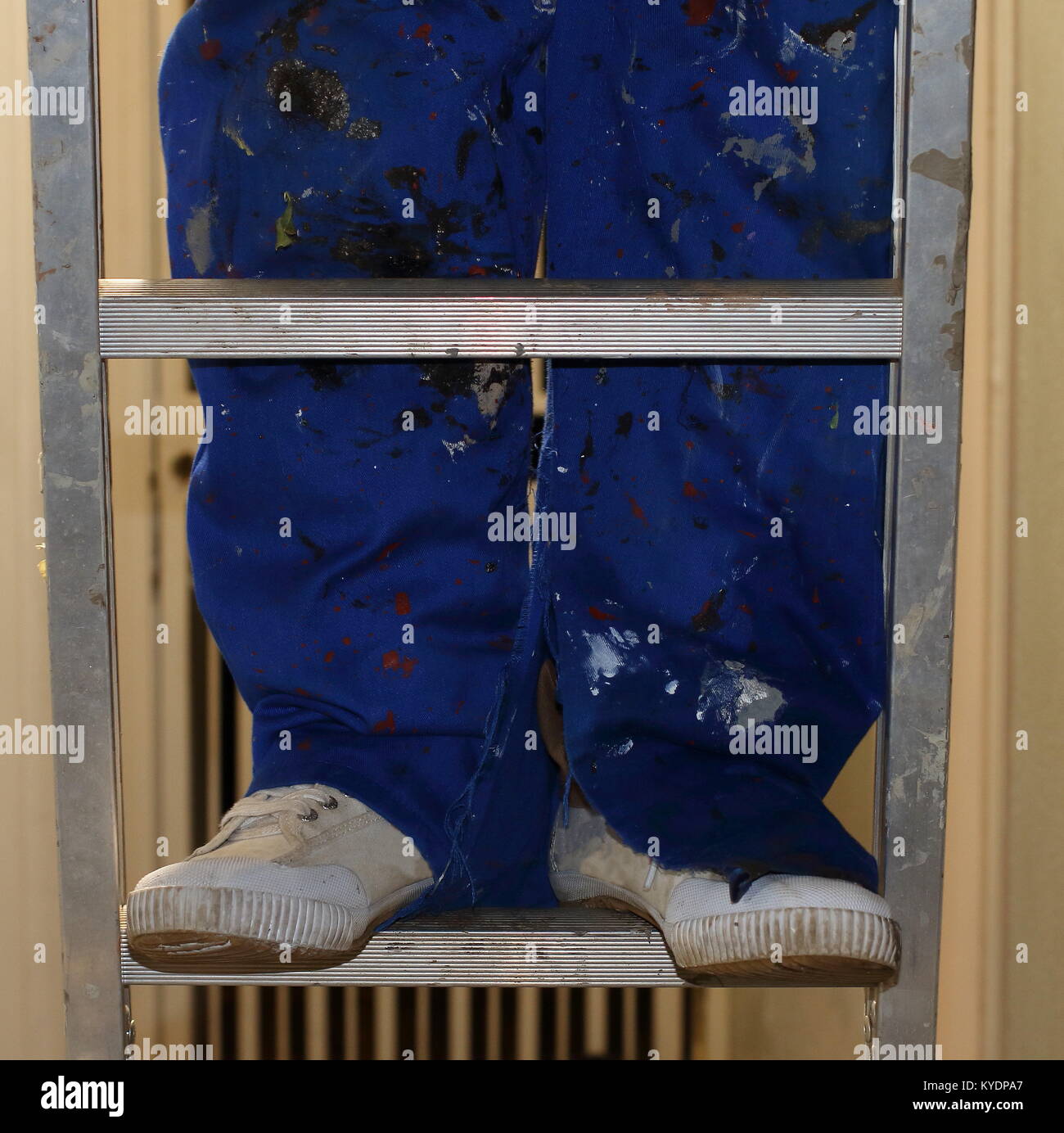 Beine in einem schmutzigen blau Farbe - insgesamt mit Canvas Schuhe stehen auf einer Leiter abgedeckt Stockfoto