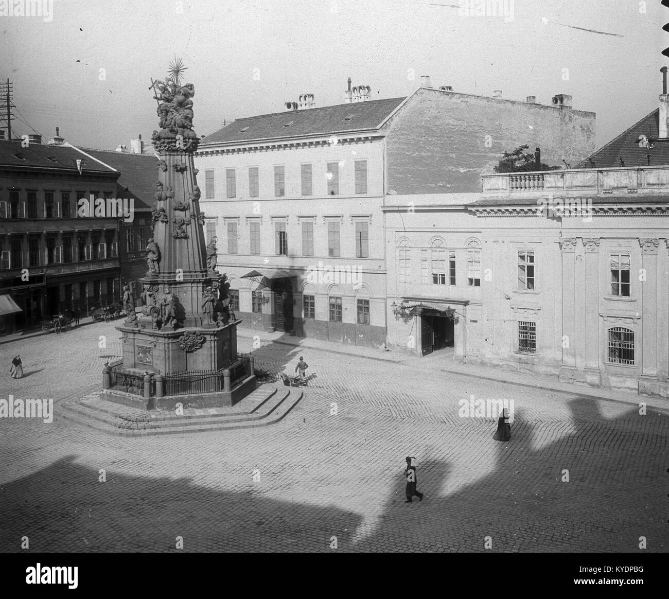Ein historischer Blick auf den Szentháromság-Platz in Budapest, Ungarn, mit der Statue der Heiligen Dreifaltigkeit und der Kreuzung der Országház-Straße im Hintergrund. Das Bild zeigt die städtische und architektonische Umgebung des Burgviertels Buda. Stockfoto