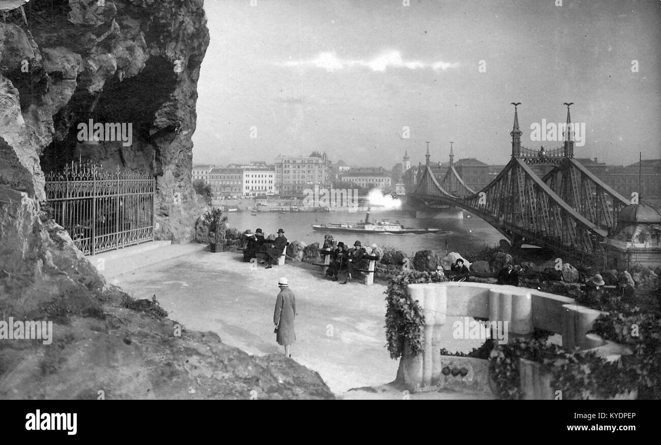 Ein historisches Foto, das die Gellért-Höhle-Kirche (Sziklakápolna) in Budapest, Ungarn, mit der Freiheitsbrücke (ehemals Franz-Joseph-Brücke) im Hintergrund zeigt. Stockfoto