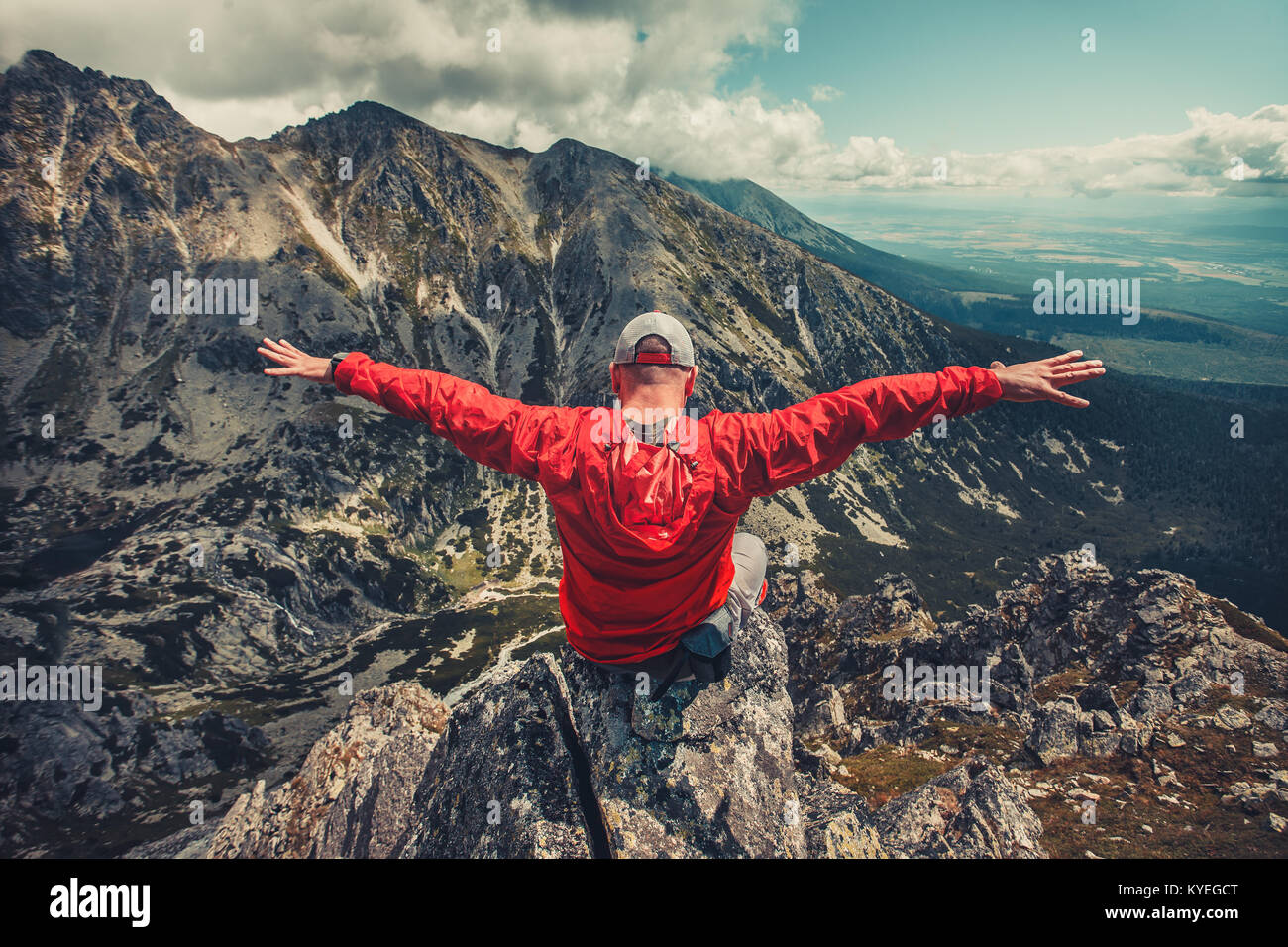 Ein Wanderer in Outdoor rot Windbreaker Jacke geniesst die herrliche Aussicht am Rande des Abgrunds in den Bergen der Hohen Tatra in der Slowakei sitzen. Das Gefühl Stockfoto