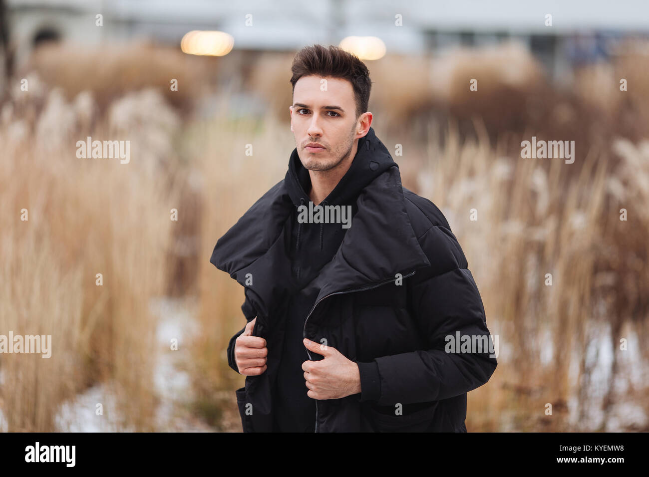 Stilvolle Mann wolk auf der Straße. Winter kalt Outfit. Große Jacke mit weißen Turnschuhen. Blured Hintergrund Straße. Profecional Modell Foto. Stockfoto