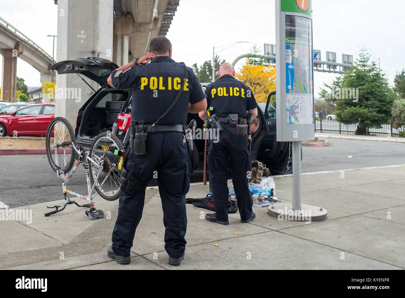 Zwei Bay Area Rapid Transit (BART) Polizisten von hinten gesehen, mit einem Umgeworfen, Fahrrad- und Beutel mit sortiert Schmuggelware auf dem Bürgersteig vor der Offiziere, die in der San Francisco Bay Area Stadt von Daly City, Kalifornien, November 3, 2017. () Stockfoto