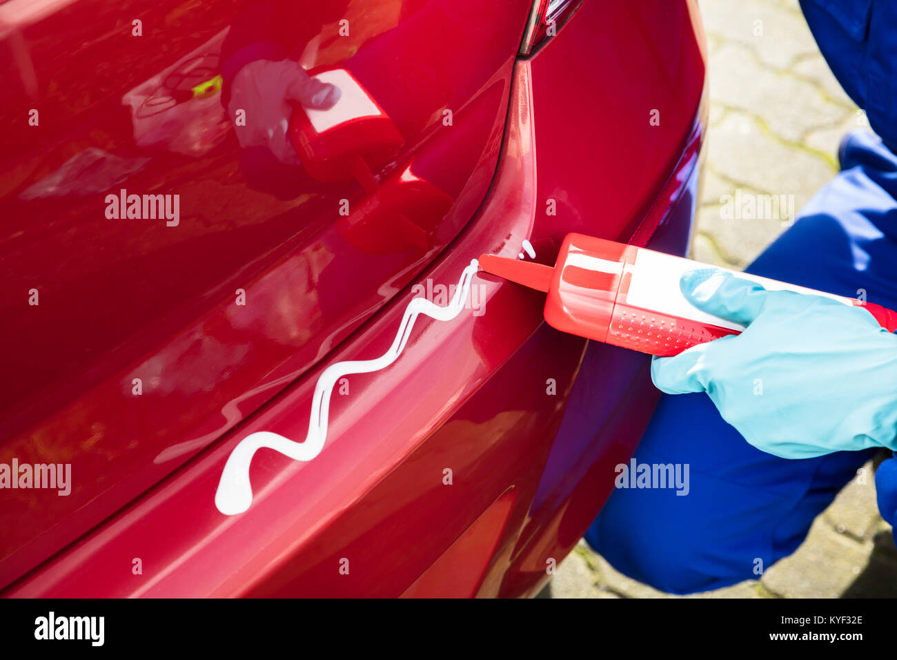 Person's Hand mit Handschuhen Anwendung sauberer Compound mit Flasche auf dem Auto Stockfoto