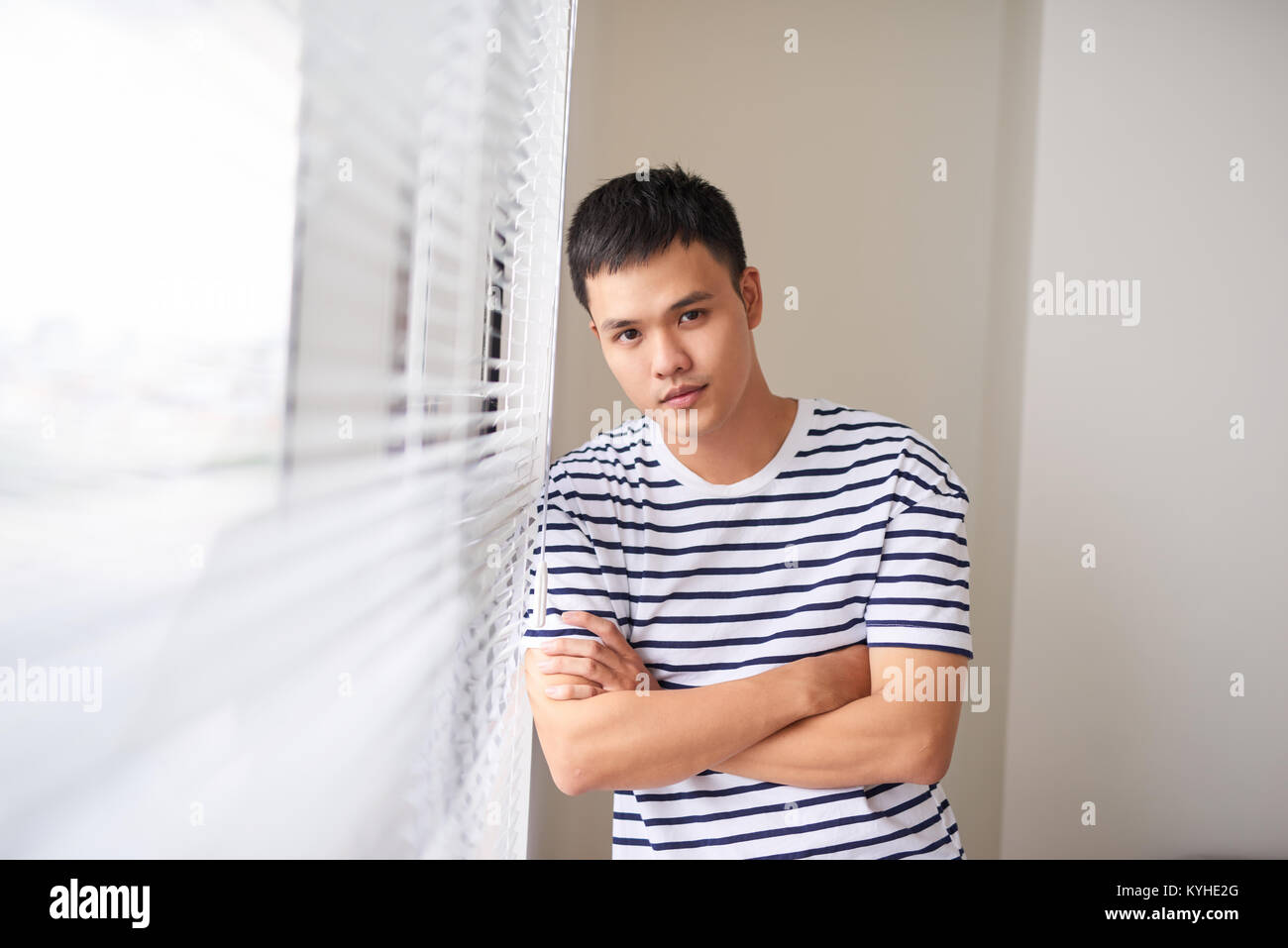 Porträt eines jungen Mannes mit gekreuzten Händen in der Nähe der Fenster. Stockfoto