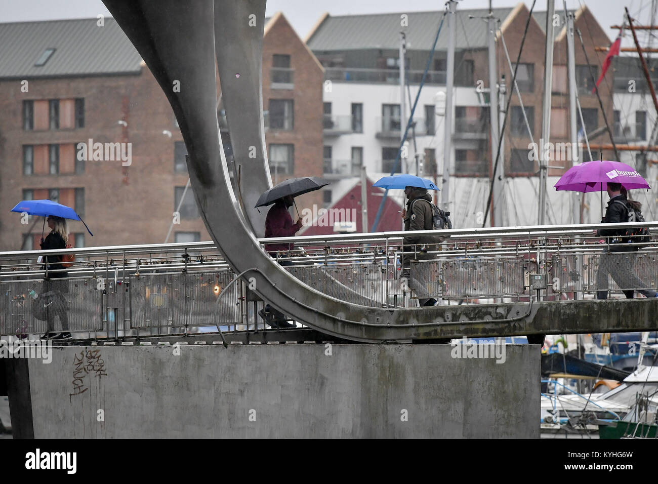 Menschen Schutz unter Sonnenschirmen im strömenden Regen, da sie Pendeln über die Millennium Bridge, Bristol, auf was behauptet wird der traurigste Tag des Jahres, um arbeiten zu können. Stockfoto
