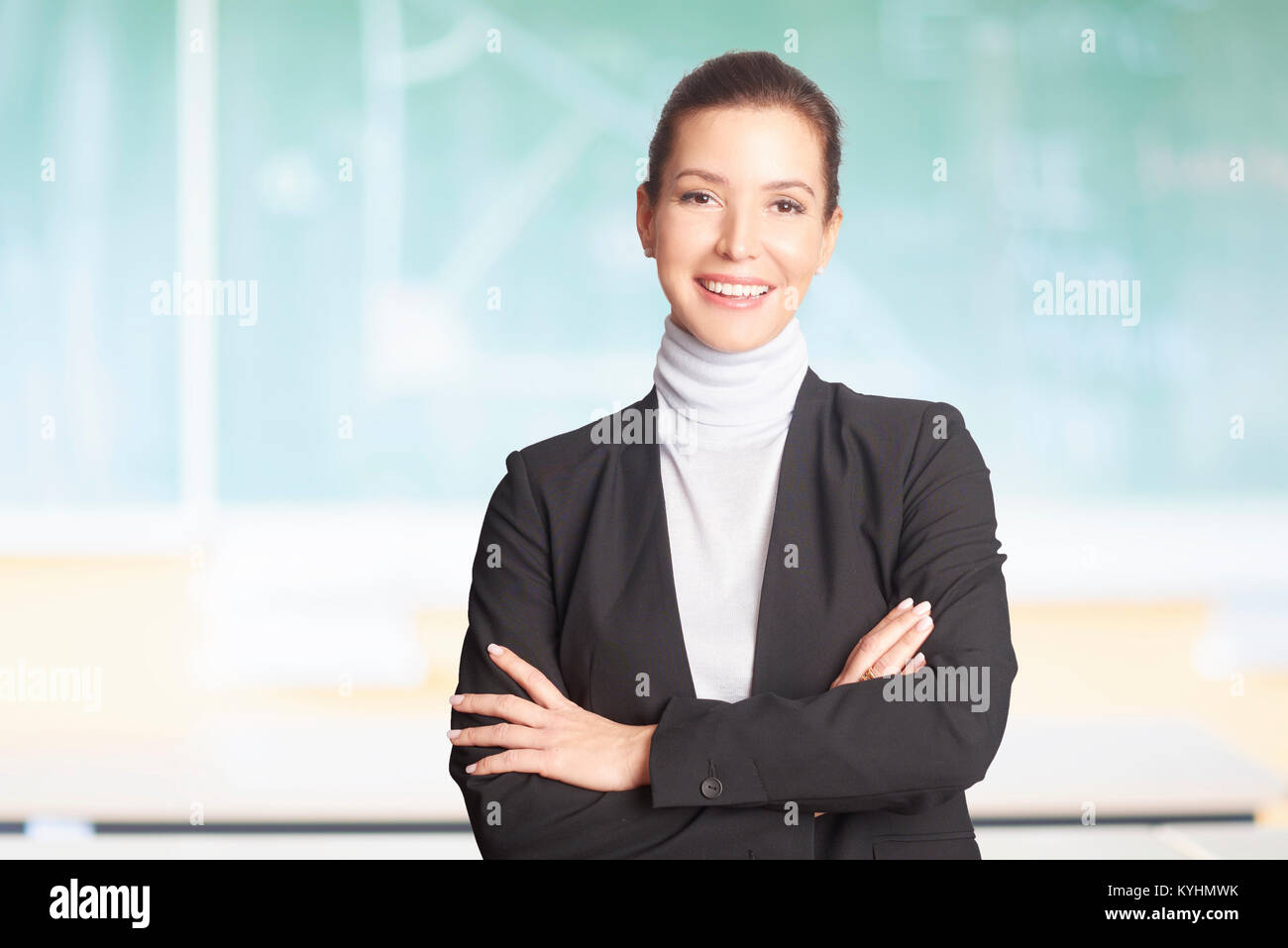 Eine schöne Lehrerin stand mit verschränkten Armen vor der Tafel im Klassenzimmer gekreuzt. Stockfoto