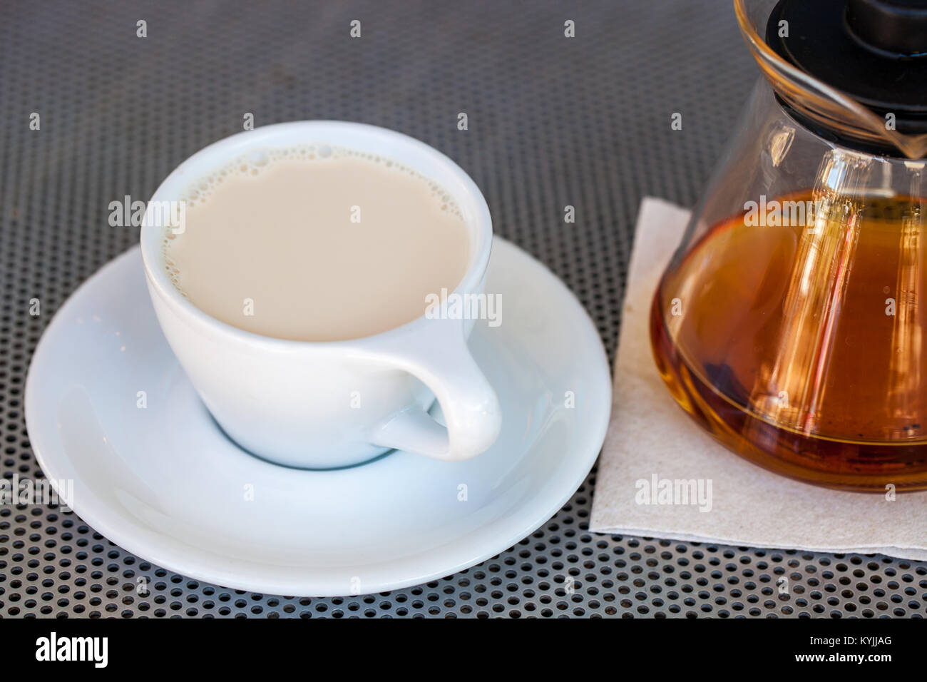 Selektiver Fokus von schwarzem Tee mit Milch in weißem Porzellan Tasse mit Teekanne Neben auf metallischem Tabelle Stockfoto