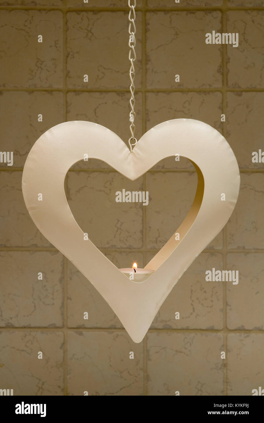 Brennendes Teelicht Kerze in Herzform metall Kerzenhalter hängen vor einem Fliesen- Hintergrund Stockfoto
