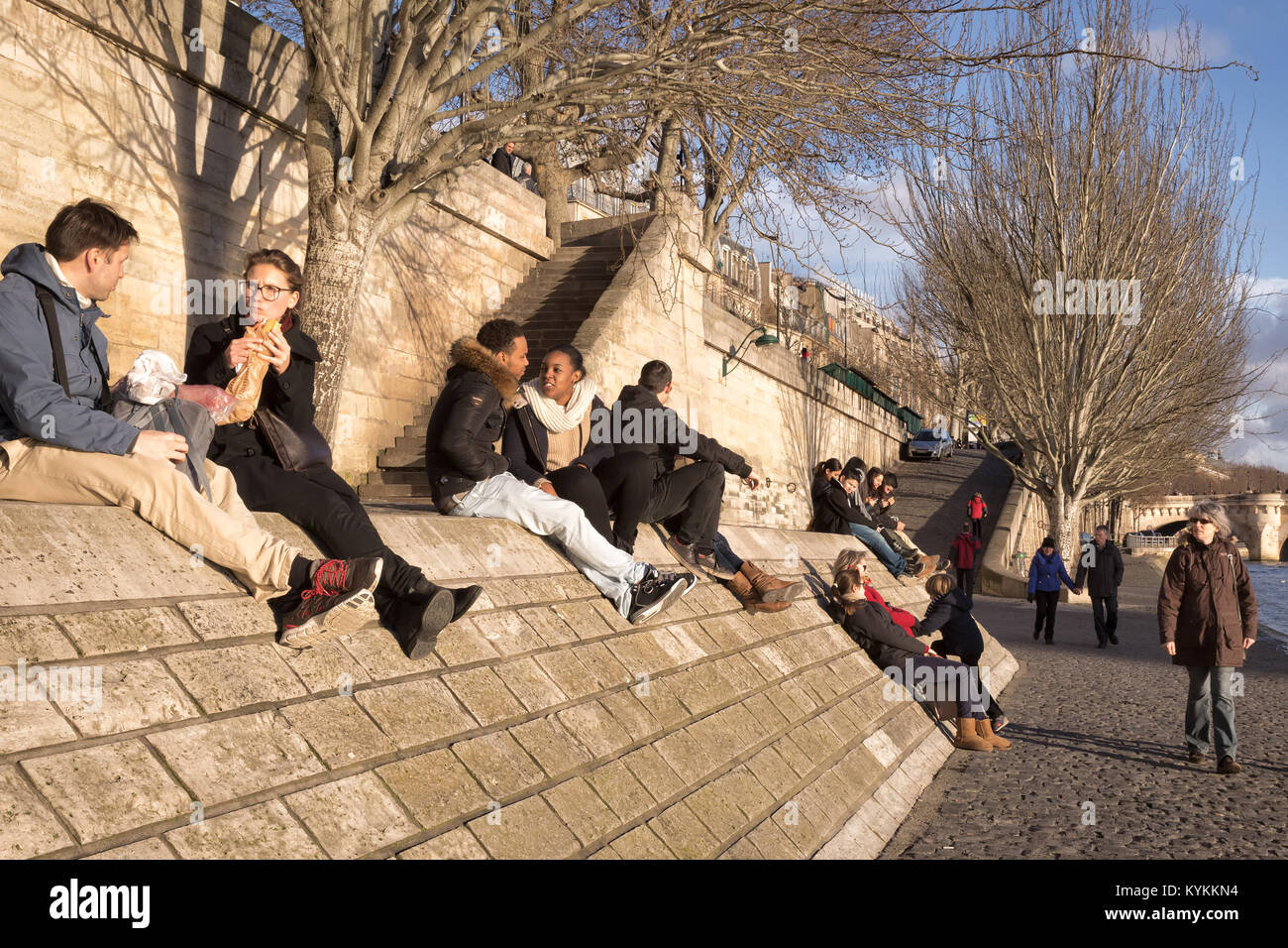 PARIS - Jan 2, 2014: Menschen sitzen am Ufer der Seine rund um den Sonnenuntergang. Paare, Familien, Freunde, essen, reden, lachen, Romantik. Stockfoto