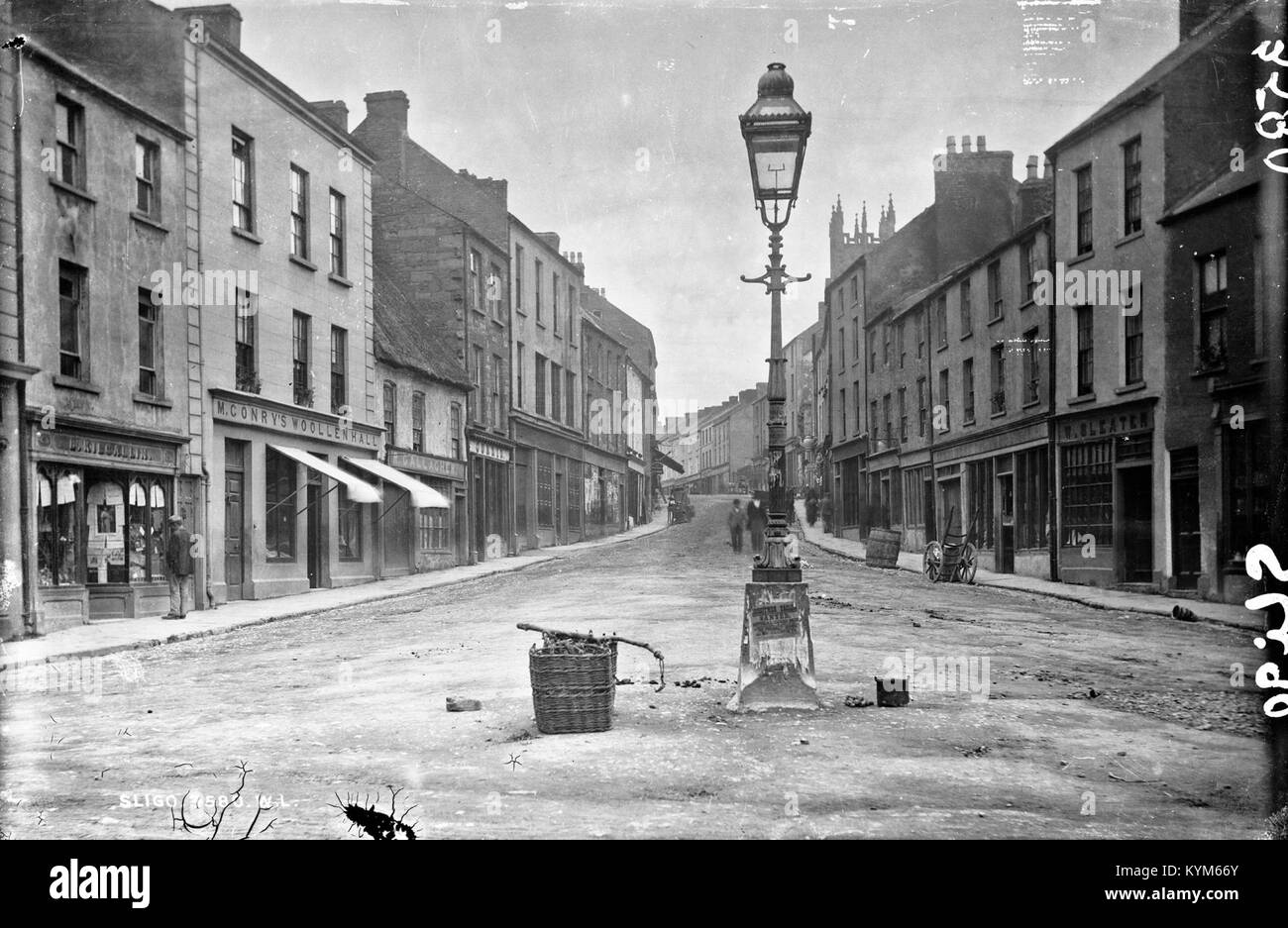 Ein historisches Glasnegativ, das eine Straßenszene in Clinchy, Co. Darstellt. Sligo, Connaught. Das Bild zeigt eine Marktstraße mit Geschäften, einem Laternenpfahl und Körben zum Verkauf. Die Fotografie ist Teil der Lawrence Collection, die Robert French im späten 19. Oder frühen 20. Jahrhundert fotografierte. Stockfoto