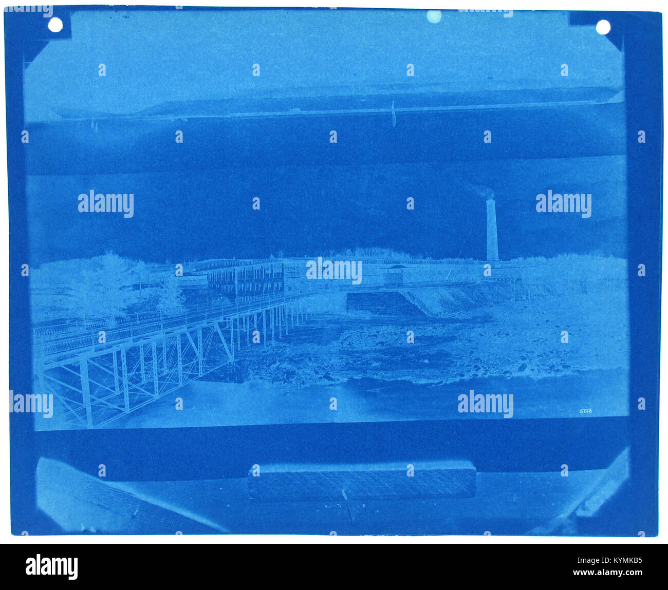 Einfarbiges Foto mit einer Brücke mit einer Fabrik und Schornsteinen im Hintergrund, aufgenommen als Fotonegativ, das eine historische Szene aus dem Archiv der Smithsonian Institution darstellt. Stockfoto