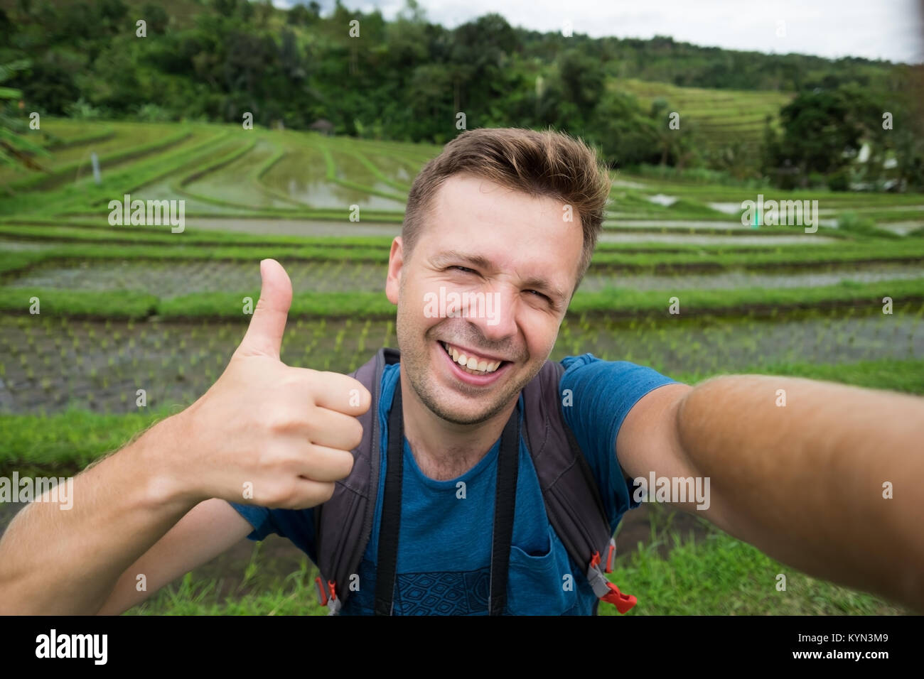 Happy kaukasischen Mann mit Rucksack Reisen in reis plantage und zeigen den Daumen nach oben. Stockfoto
