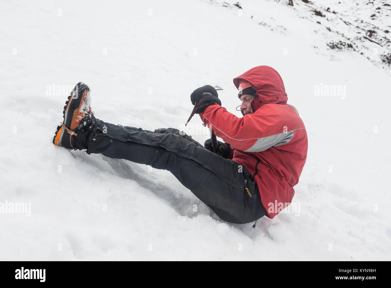 Winter Skills Training in Cairngorm Mountains vor Schnee durchlöcherte Reise Andy demonstrieren den Nutzen von Ice ax eine Folie © Paul Glendell zu verhindern Stockfoto
